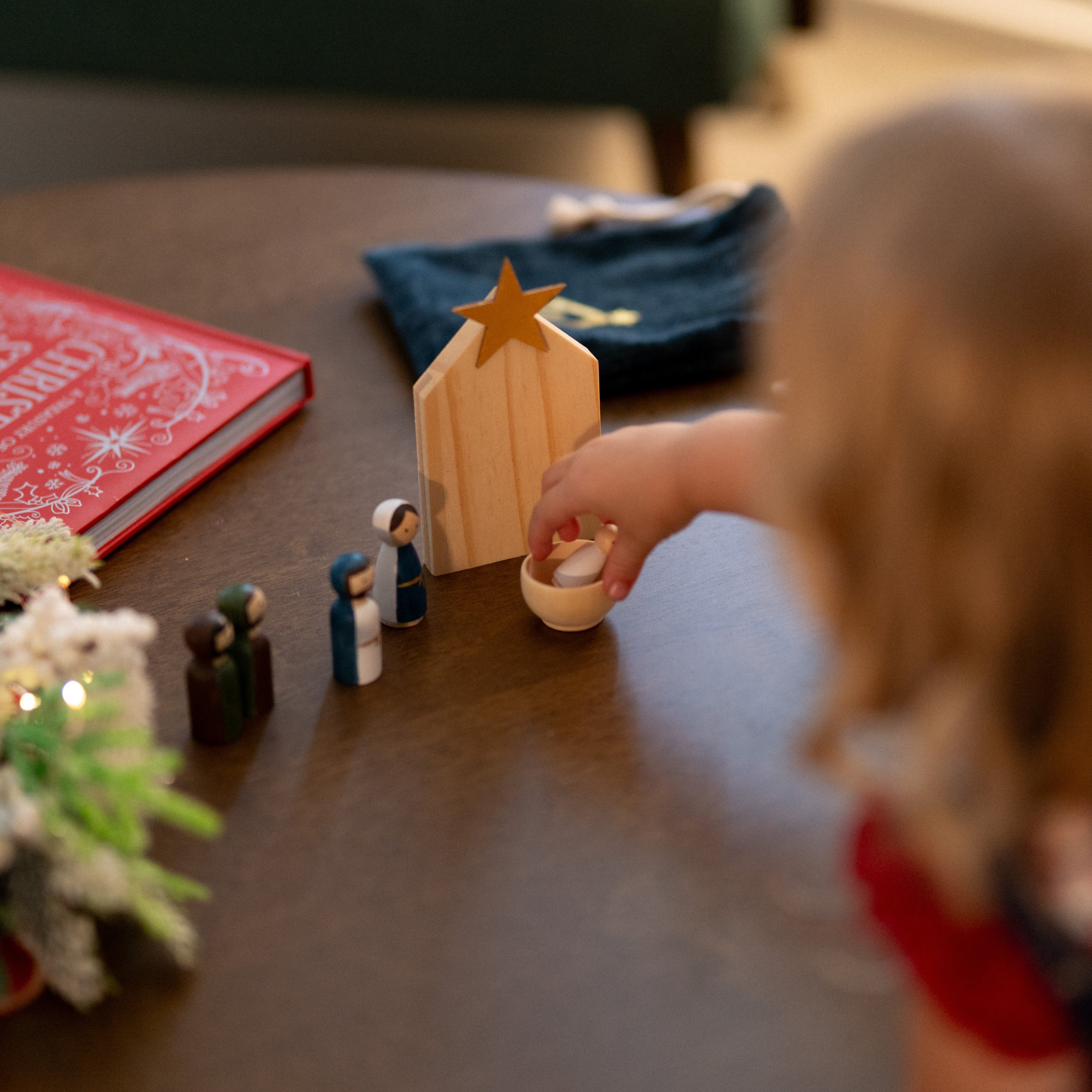 Child playing with a nativity set on a table with a blurred background