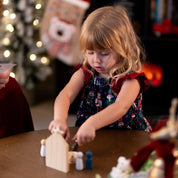 Child playing with wooden toys at a table in a festive indoor setting.