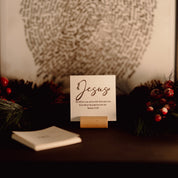 Card with 'Jesus' on a table surrounded by greenery and berries