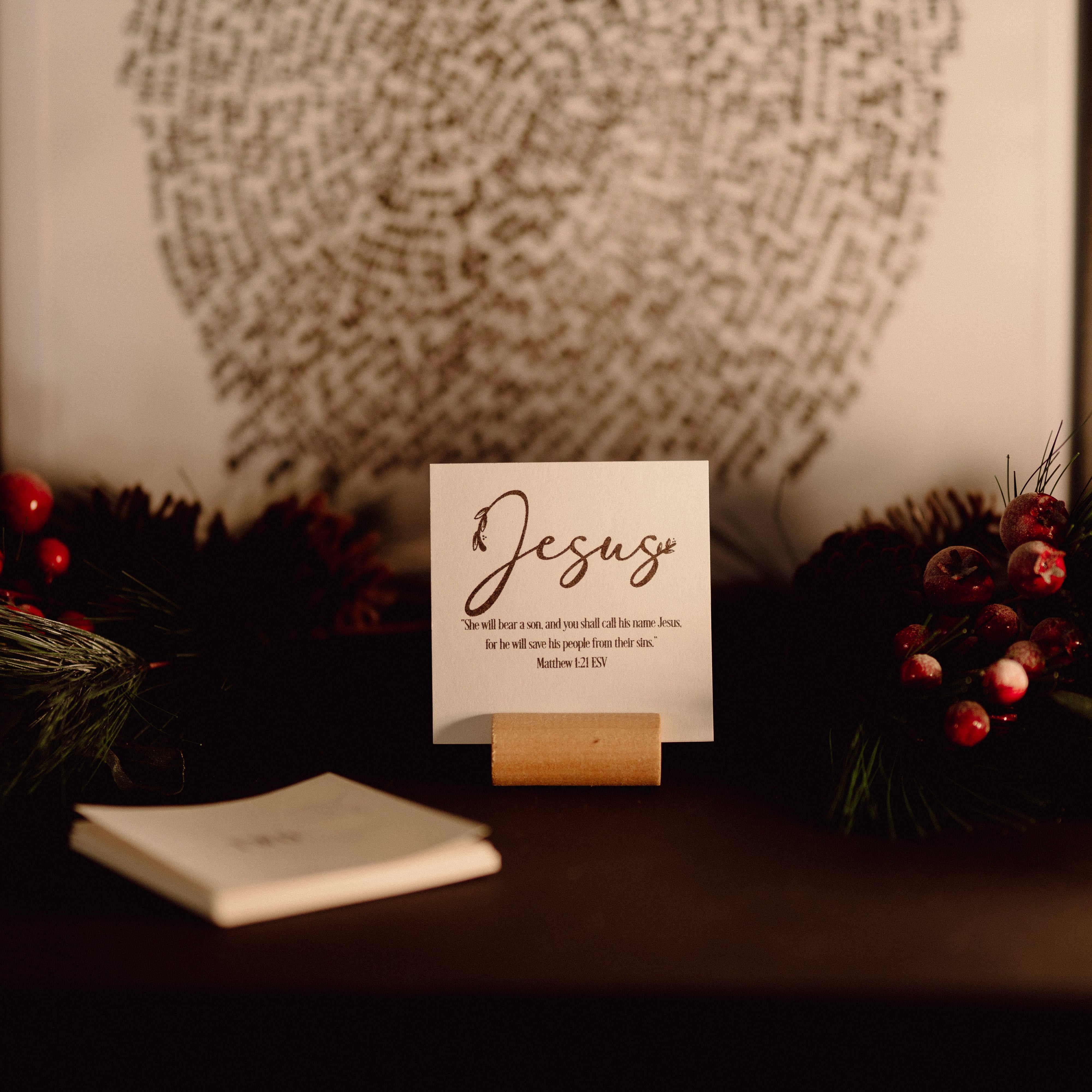 Card with 'Jesus' on a table surrounded by greenery and berries