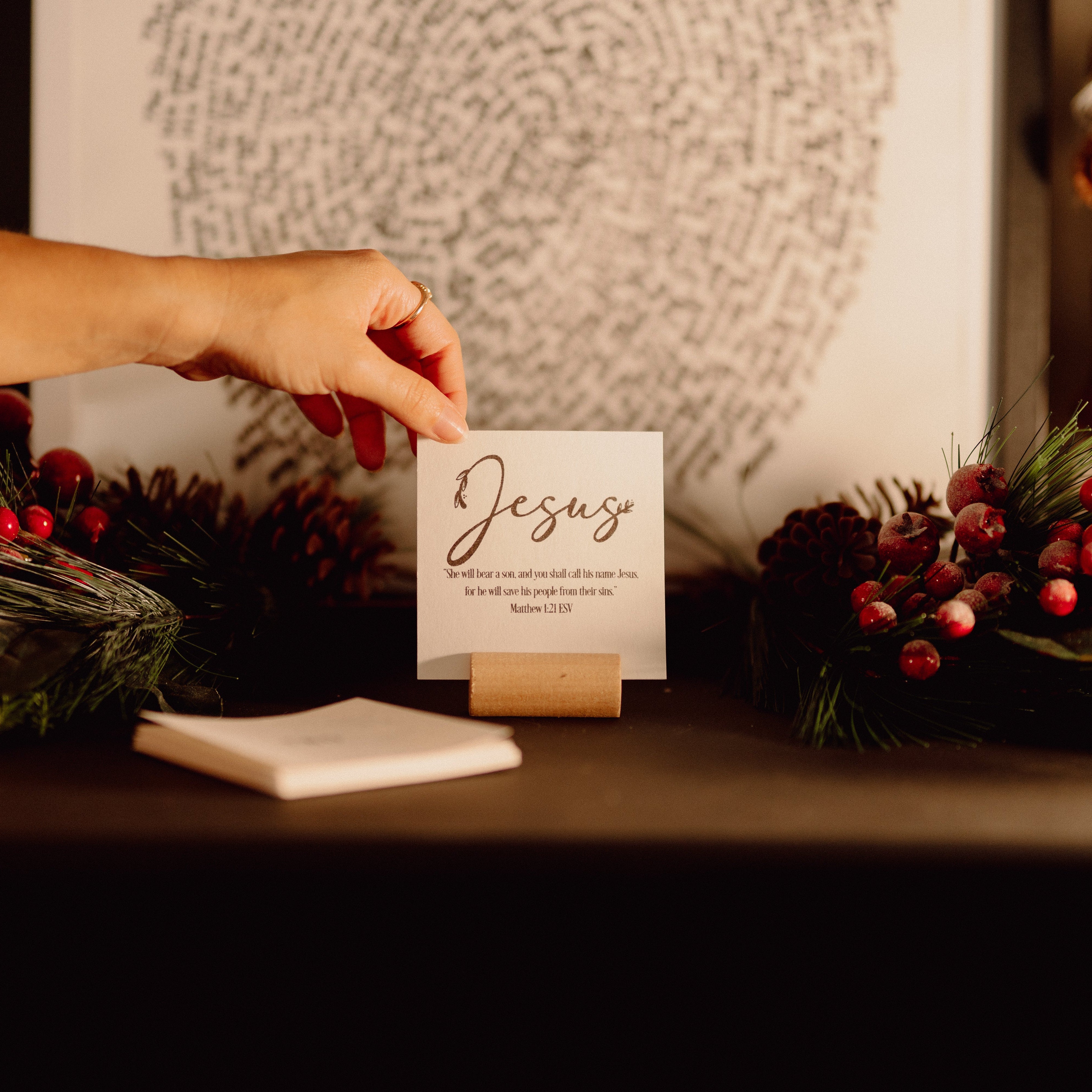 Hand placing a card with 'Jesus' on a table with Christmas decorations
